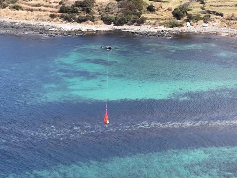 海上で荷物を吊り下げて飛行するドローン